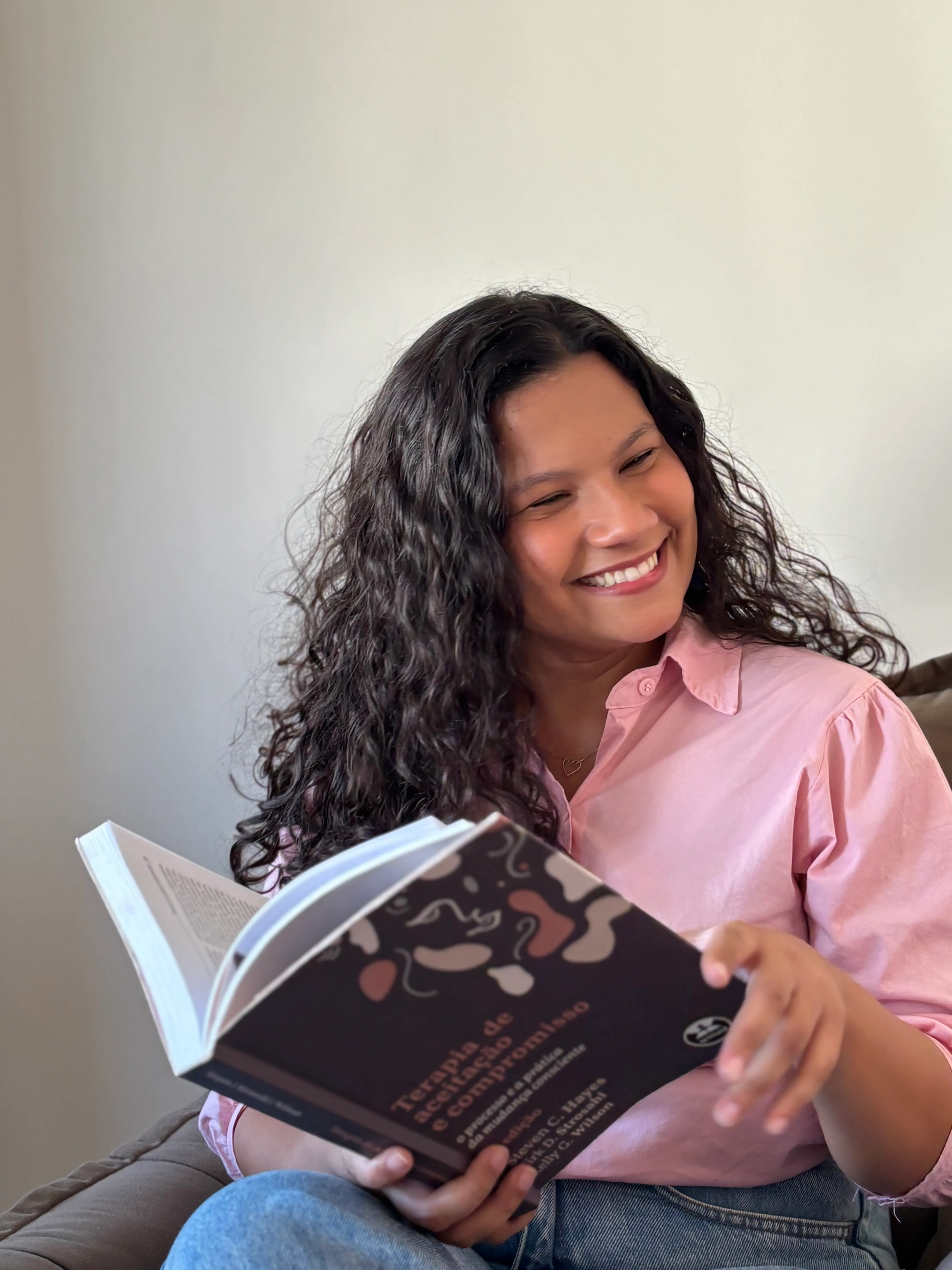 Brenda Magalhães Pereira, psicóloga, sorrindo enquanto lê em uma poltrona do consultório